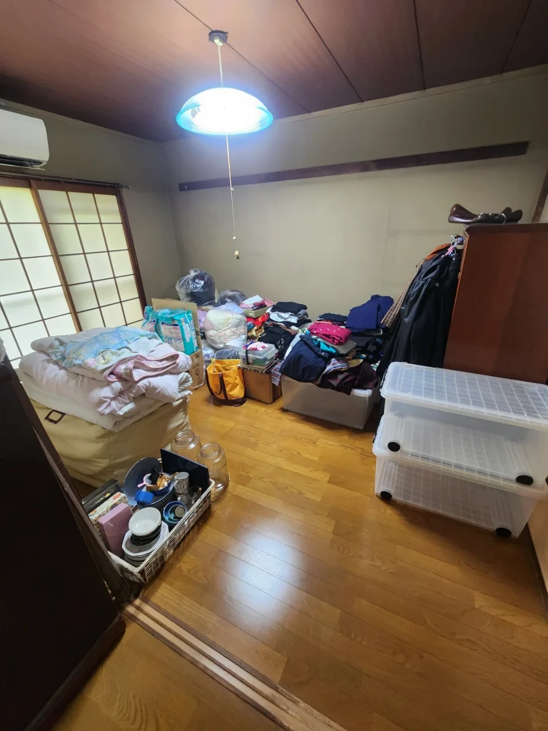 和室に積まれた布団や衣類、収納ケースの整理状況